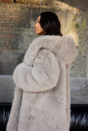 Woman wearing a light gray fur coat standing outdoors.