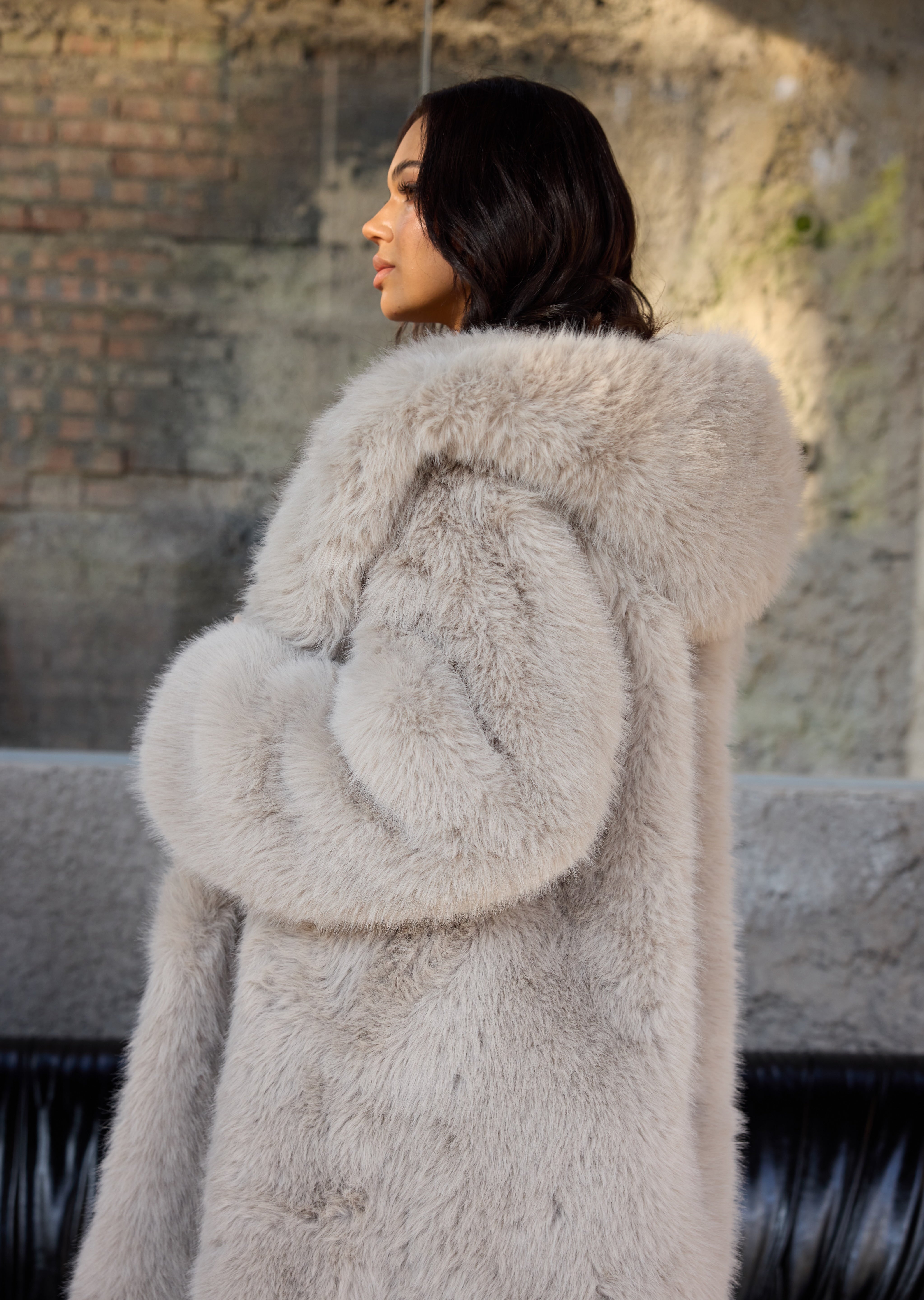 Woman wearing a light gray fur coat standing outdoors.