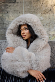 Woman wearing a fluffy gray hooded coat sitting on a stone bench.
