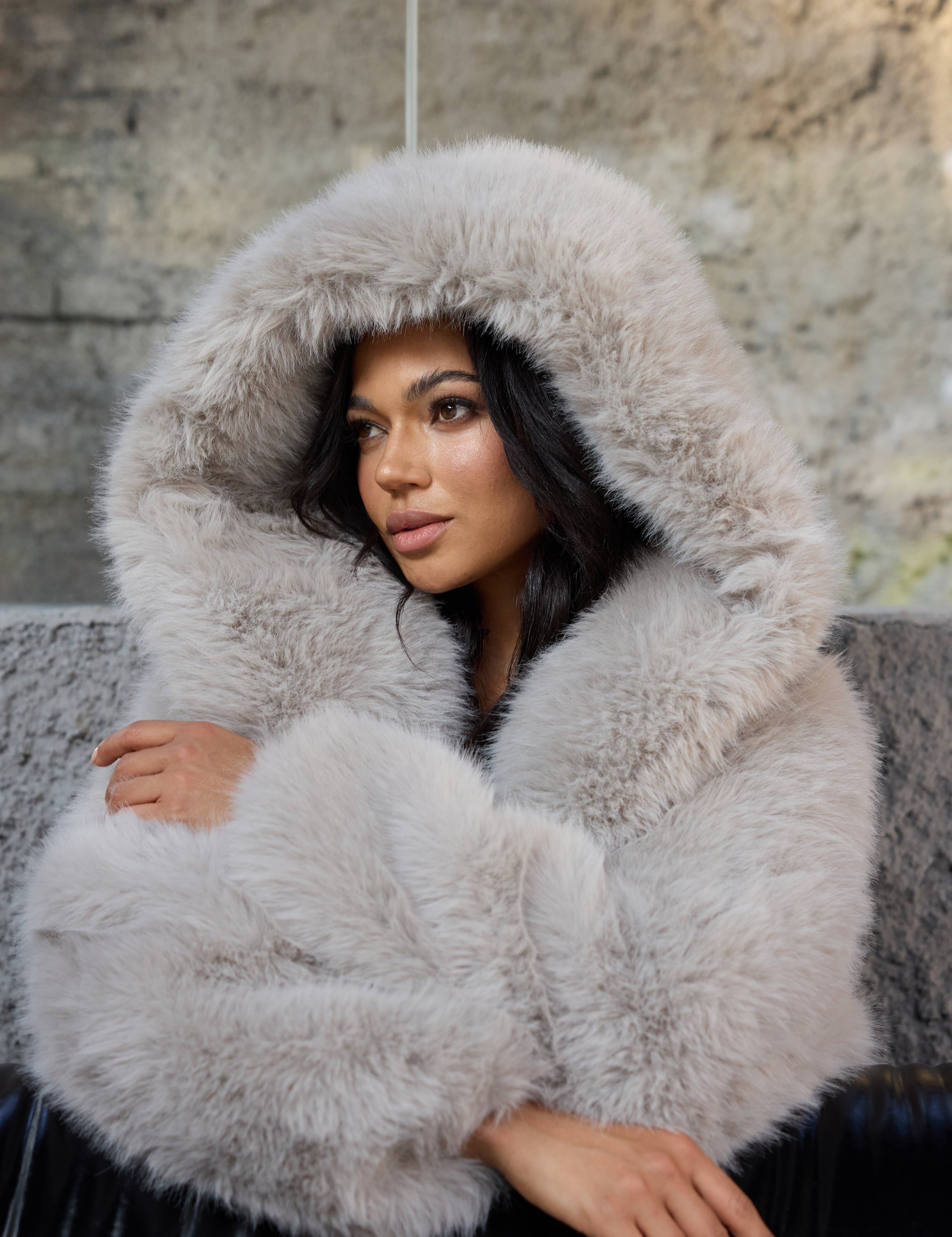 Woman wearing a fluffy gray hooded coat sitting on a stone bench.
