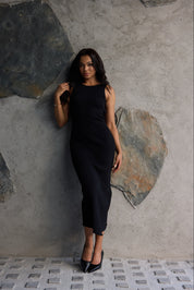 Woman in a black dress standing against a textured stone wall.