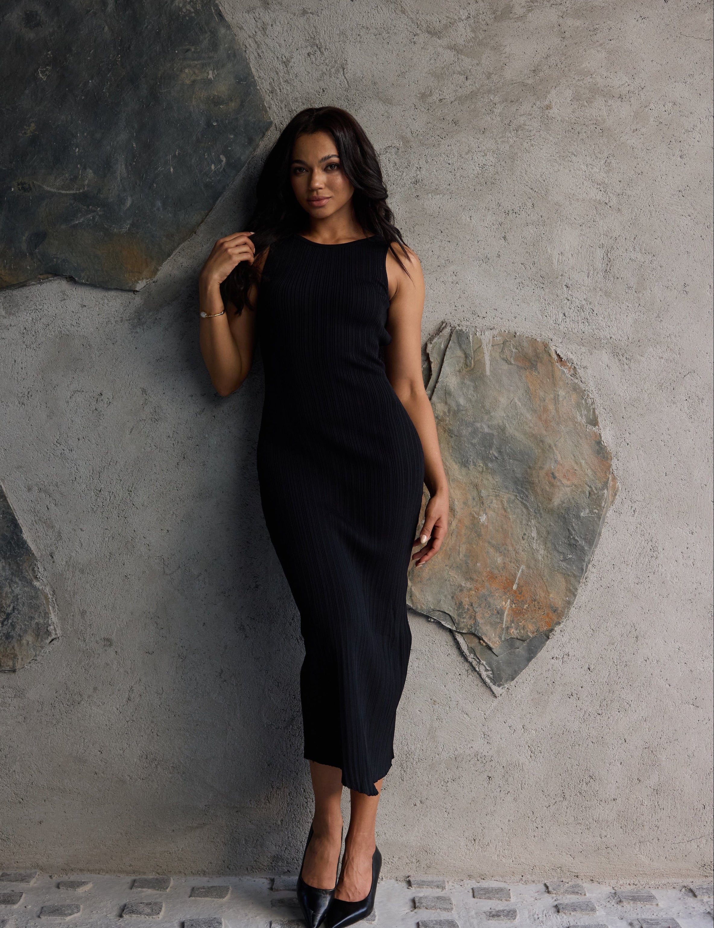 Woman in a black dress standing against a textured stone wall.