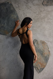 Woman in a black dress standing against a textured stone wall.